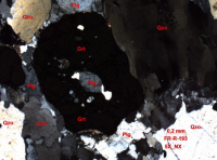 Mosaico de granada (Grt), quartzo (Qzo), onde a granada (Grt) engloba cristais de plagioclásio (Plg) e quartzo (Qzo), observando-se forte extinção ondulante no quartzo (Qzo). Aumento de 5_NX (RIBEIRO; MORAES, CBPM 2015).